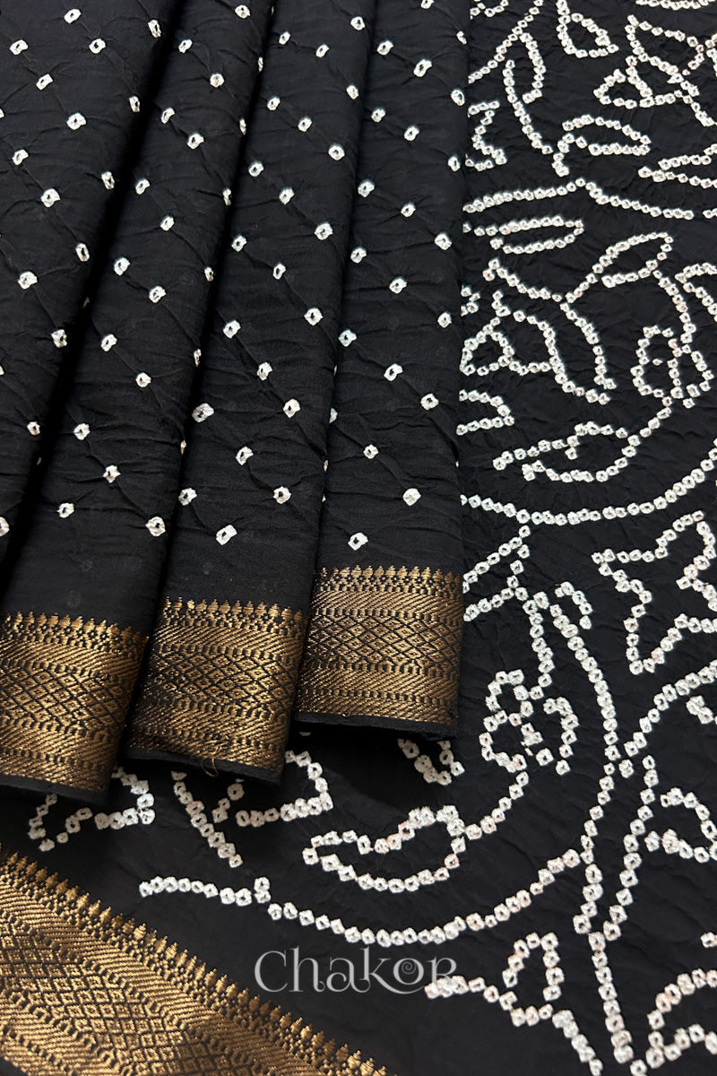 Close-up of black saree, arranged in pleats with rai bandhani and golden border showcasing beautiful craftsmanship.
