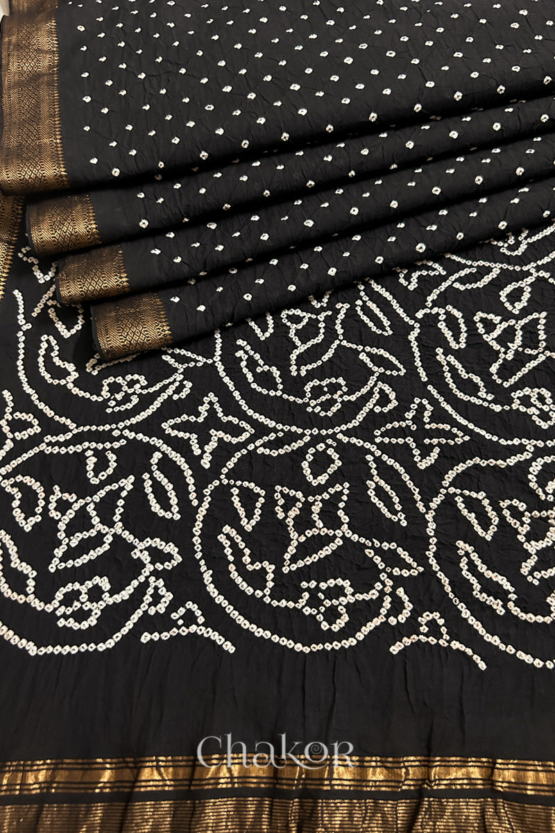 Close-up of black saree, arranged in pleats with rai bandhani and golden border showcasing beautiful craftsmanship.
