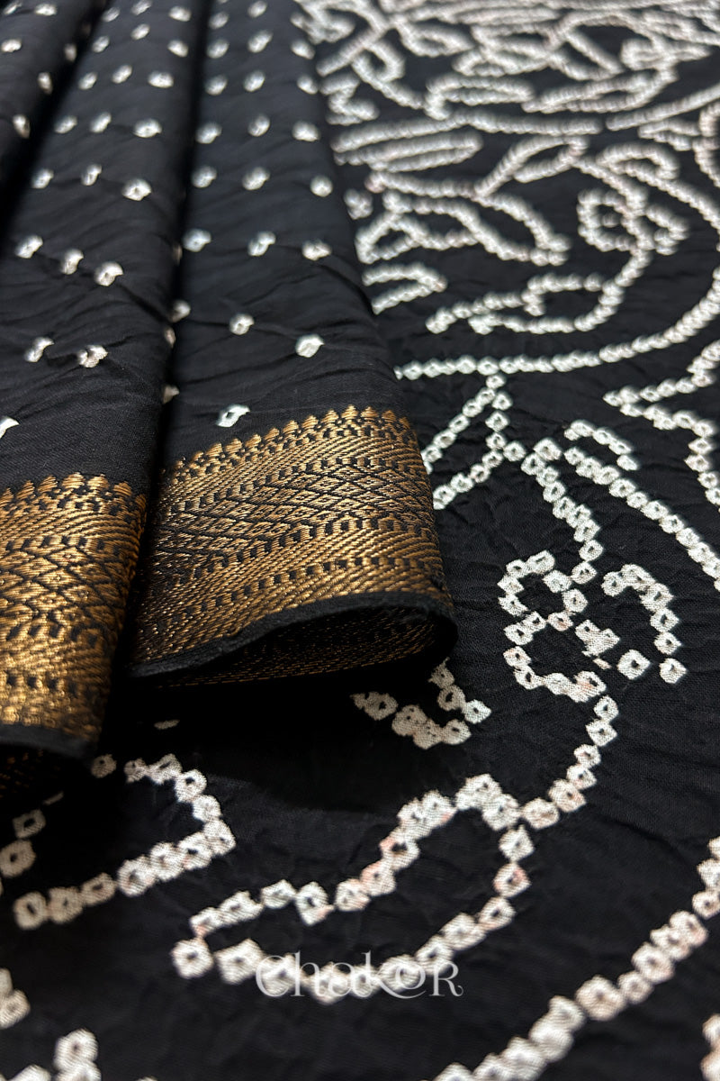 Close-up of black saree with rai bandhej showcasing intricate tie-dye craftsmanship with golden border and fabric texture.
