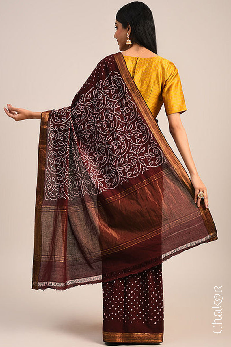 Woman wearing a maroon bandhani saree showcasing intricate tie dye design on pallu and zari border.