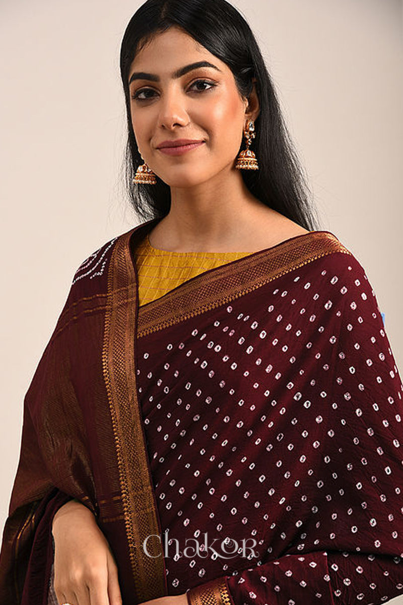 Woman wearing a maroon bandhej saree with white bandhani dots and golden border.