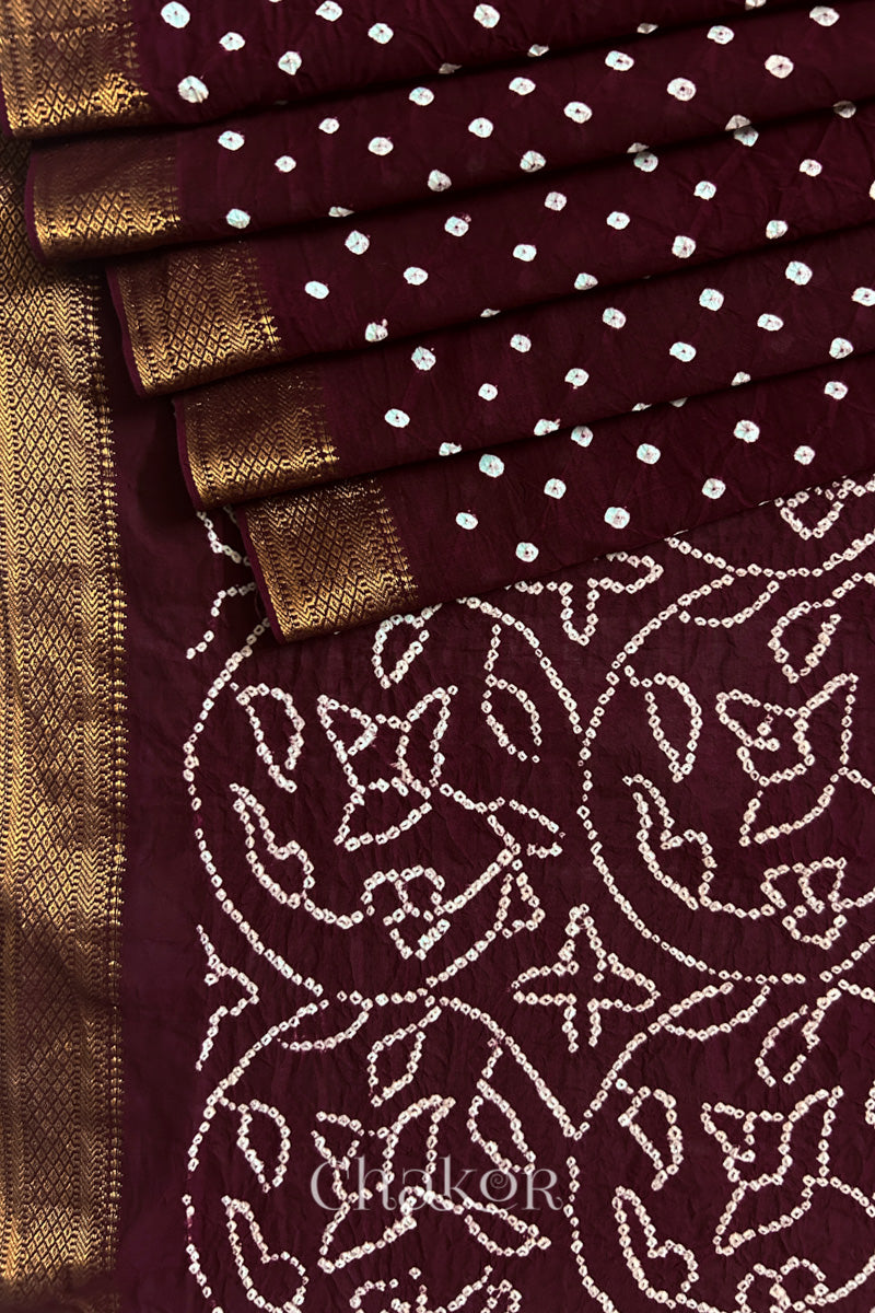 Close-up of maroon saree, arranged in pleats with rai bandhani and golden border showcasing beautiful craftsmanship.
