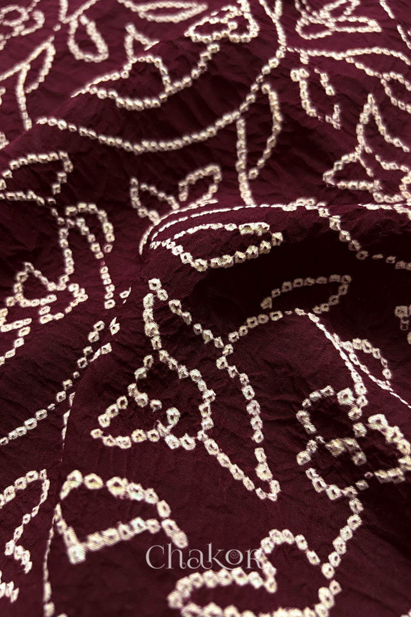 Close-up of maroon saree with rai bandhej showcasing intricate tie-dye craftsmanship and fabric texture.
