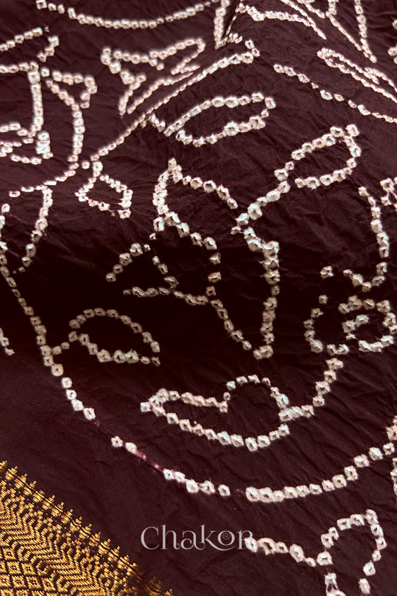 Close-up of maroon saree with rai bandhej showcasing intricate tie-dye craftsmanship and fabric texture.
