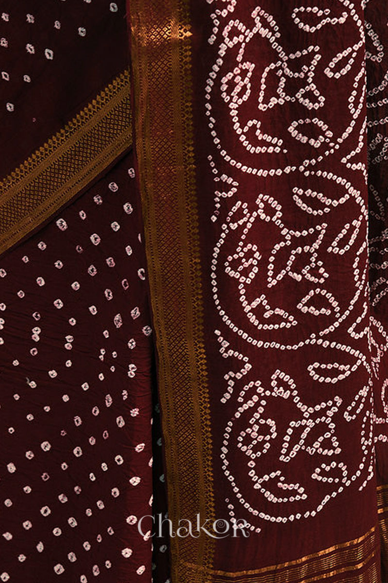Close-up of maroon saree with rai bandhej pallu and golden border showcasing intricate tie-dye craftsmanship.
