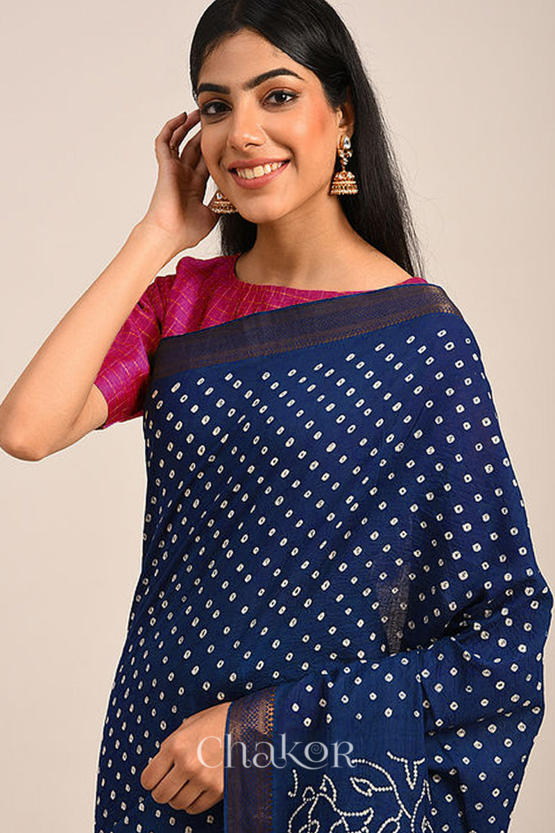Woman wearing a navy blue bandhej saree with white bandhani dots and golden border.