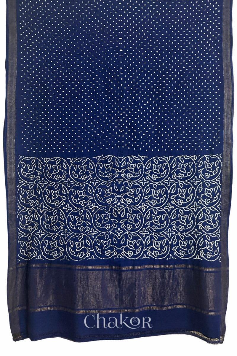 Navy blue saree, flat draped with Rai Bandhej traditional design against white background and 'Chakor' watermark.
