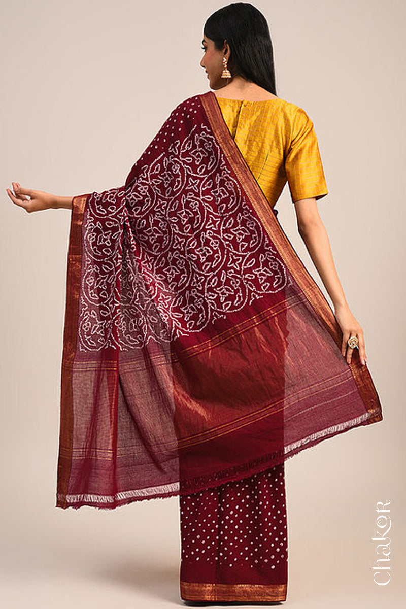 Woman wearing a deep red bandhani saree showcasing intricate tie dye design on pallu and zari border.