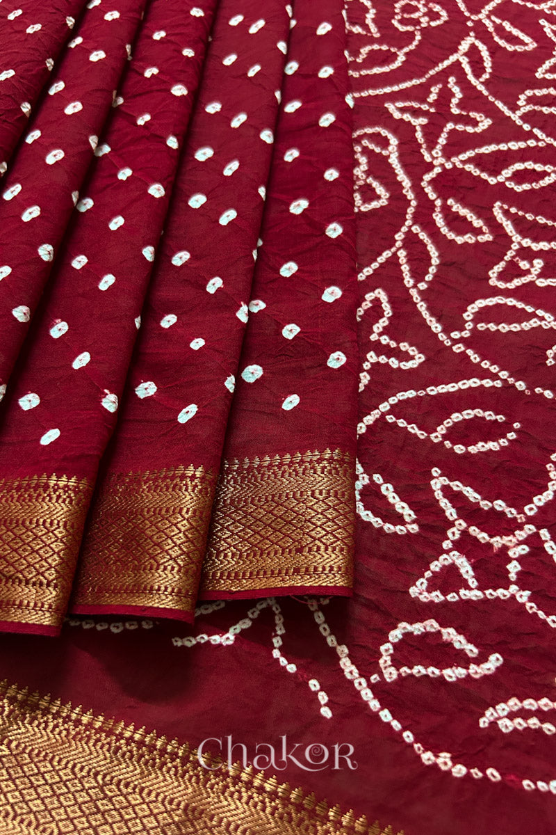 Close-up of red saree, arranged in pleats with rai bandhani and golden border showcasing beautiful craftsmanship.
