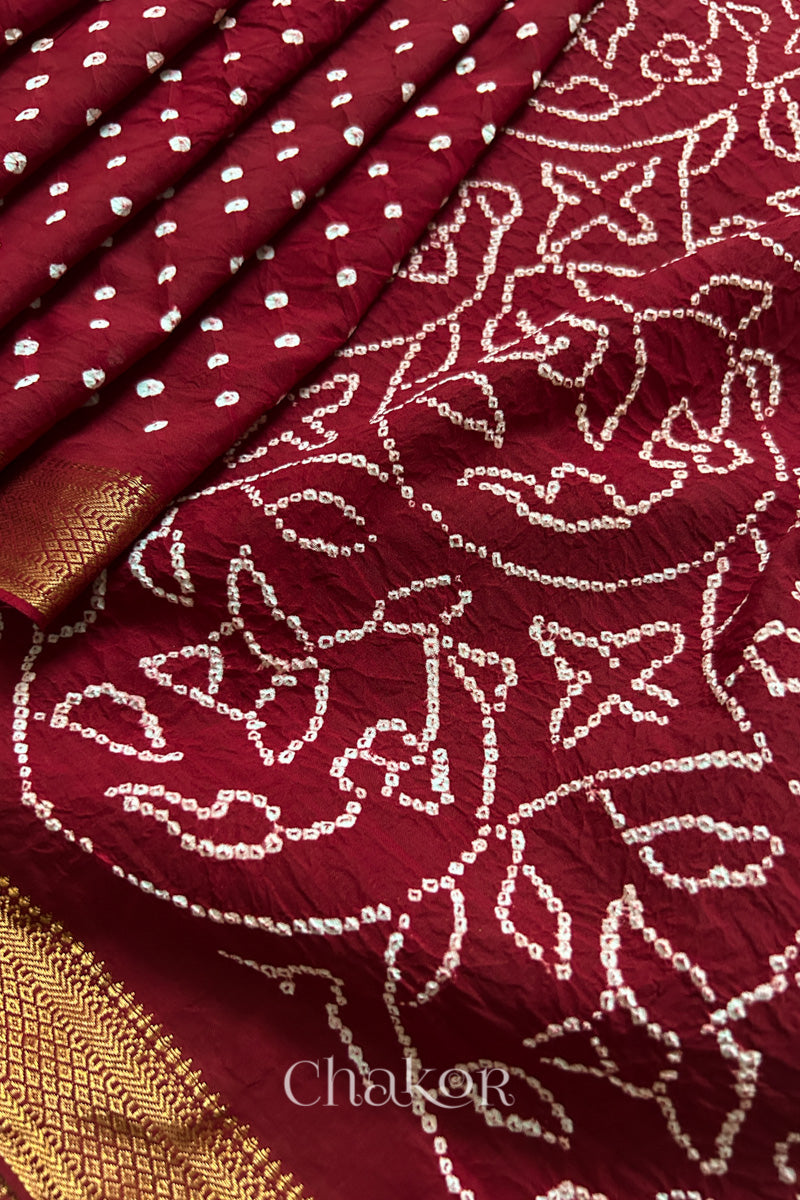 Close-up of red saree, arranged in pleats with rai bandhani and golden border showcasing beautiful craftsmanship.
