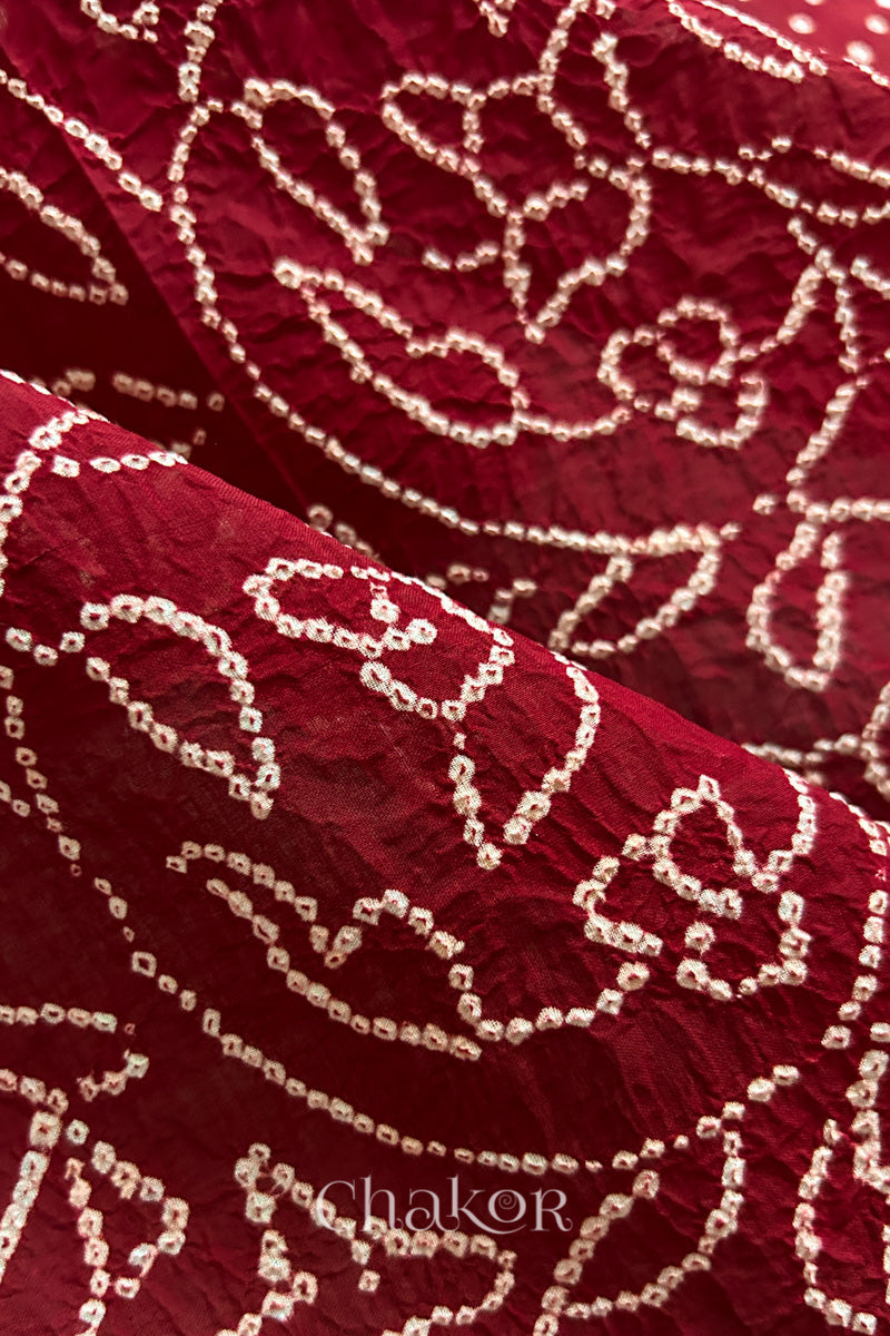 Close-up of red saree with rai bandhej showcasing intricate tie-dye craftsmanship and fabric texture.
