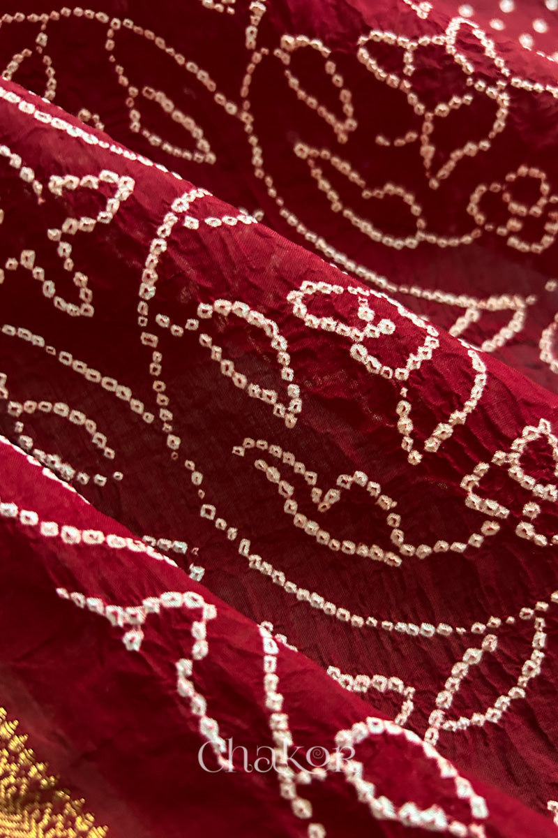 Close-up of red saree with rai bandhej showcasing intricate tie-dye craftsmanship and fabric texture.
