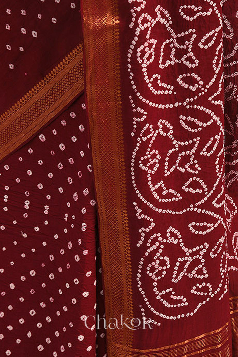 Close-up of red saree with rai bandhej pallu and golden border showcasing intricate tie-dye craftsmanship.
