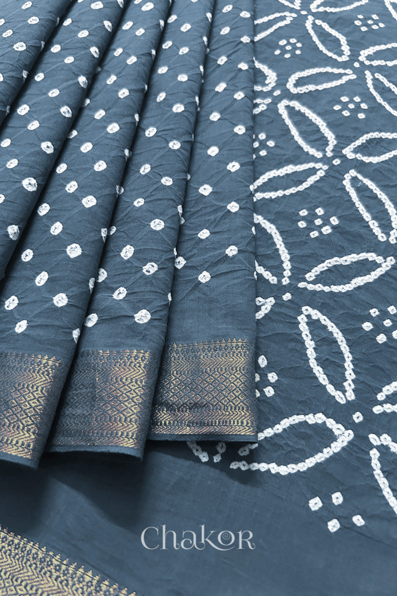Close-up of grey saree, arranged in pleats with rai bandhani and golden border showcasing beautiful craftsmanship.
