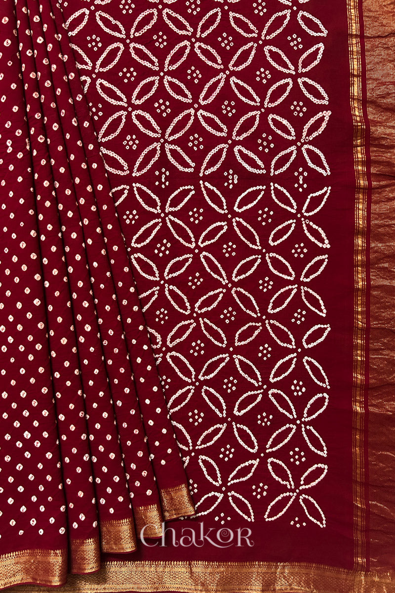Red saree, neatly arranged in pleats with Rai Bandhej traditional design and 'Chakor' brand watermark.
