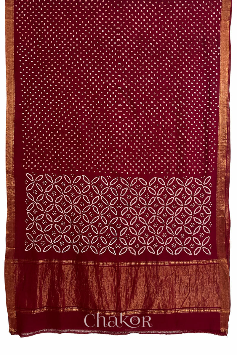 Red saree, flat draped with Rai Bandhej traditional design against white background and 'Chakor' watermark.
