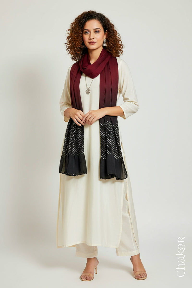 Woman wearing a maroon black shaded bandhani scarf  on white kurta set.
