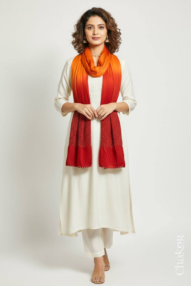 Woman wearing a orange & red shaded bandhani stole on white kurta set.

