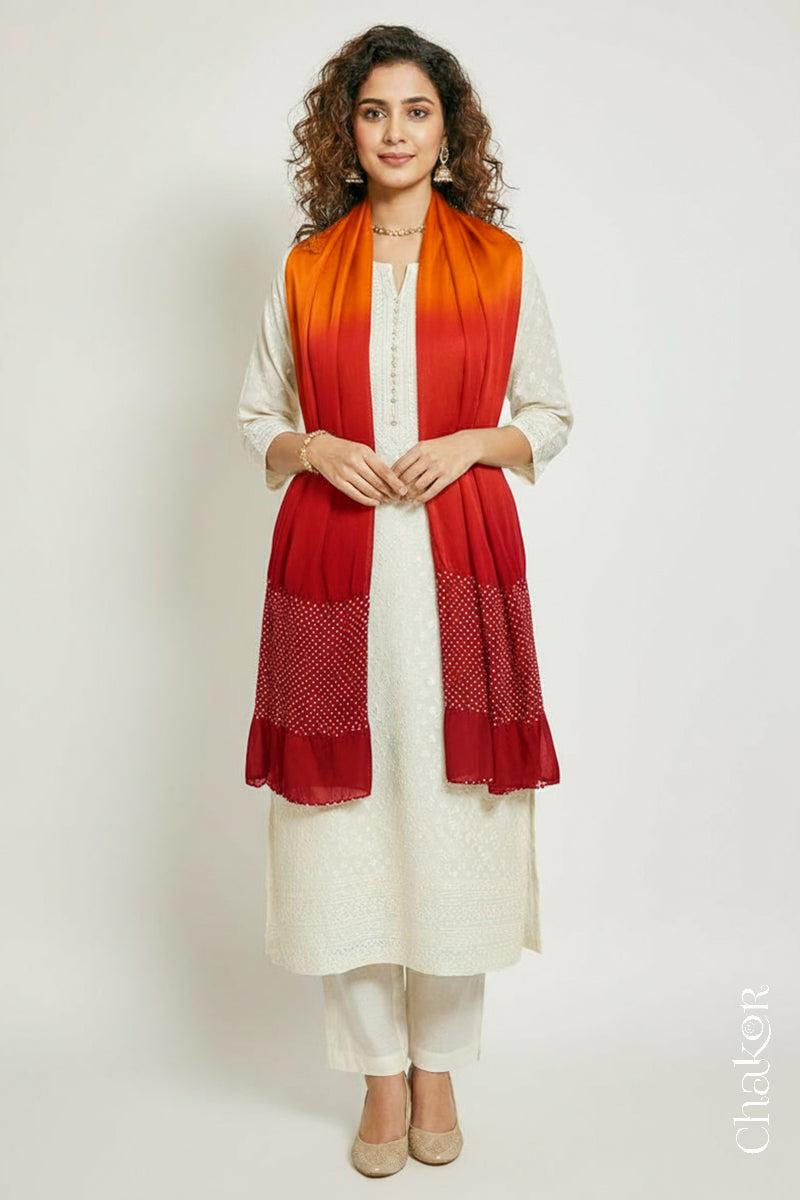 Woman wearing a orange & red shaded bandhani stole on white kurta set.
