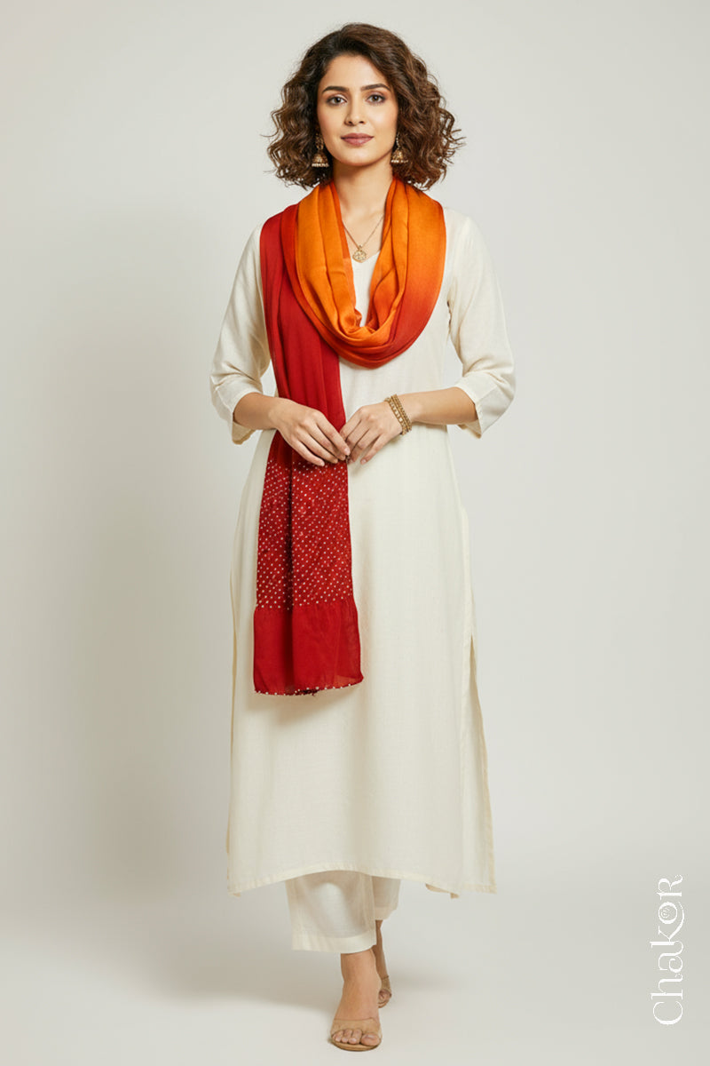 Woman wearing a orange & red shaded bandhani stole on white kurta set.
