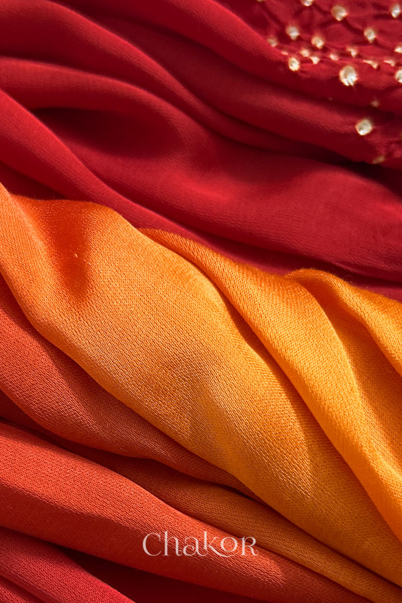 Close-up of bandhani stole featuring ombre dyeing in orange & red on lustrous modal fabric with 'Chakor' branding.

