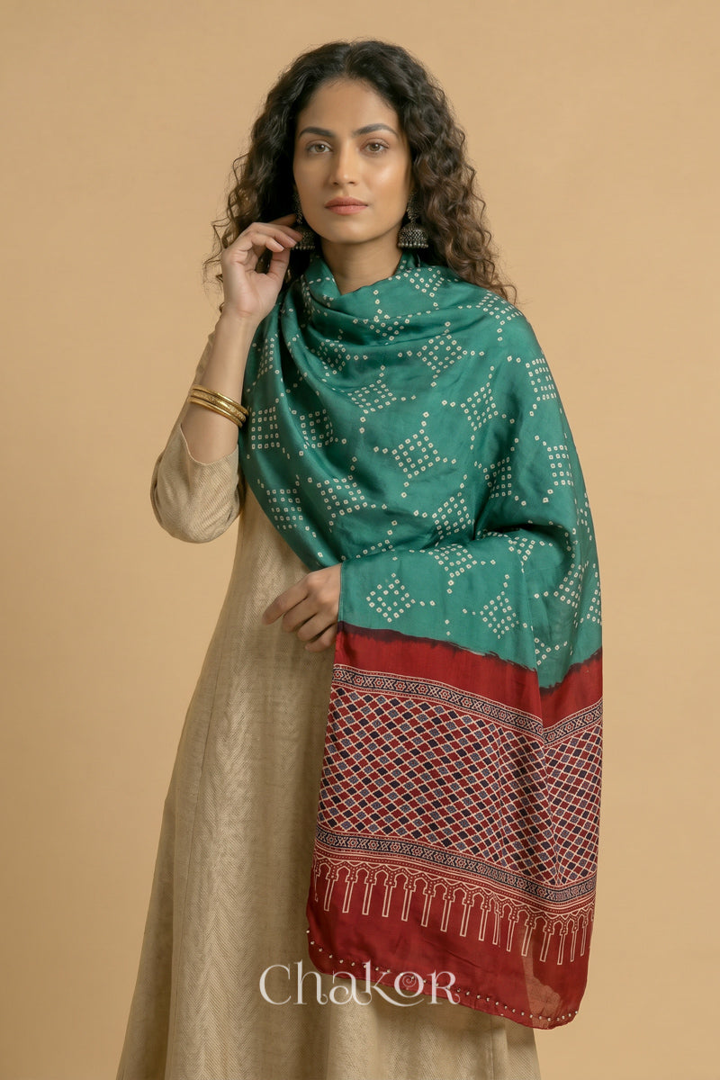 Turtle Green Bandhani modal stole styled across shoulders with detailed Madder Red Ajrakh pallu and traditional hand tied pattern.
