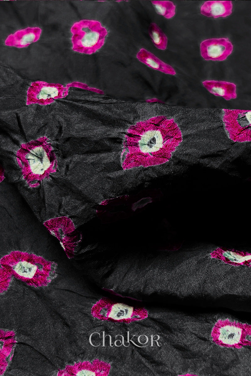 Close-up of Black fabric with Pink and white bandhani patterns, featuring texture and sheen of soft mulberry silk fabric.
