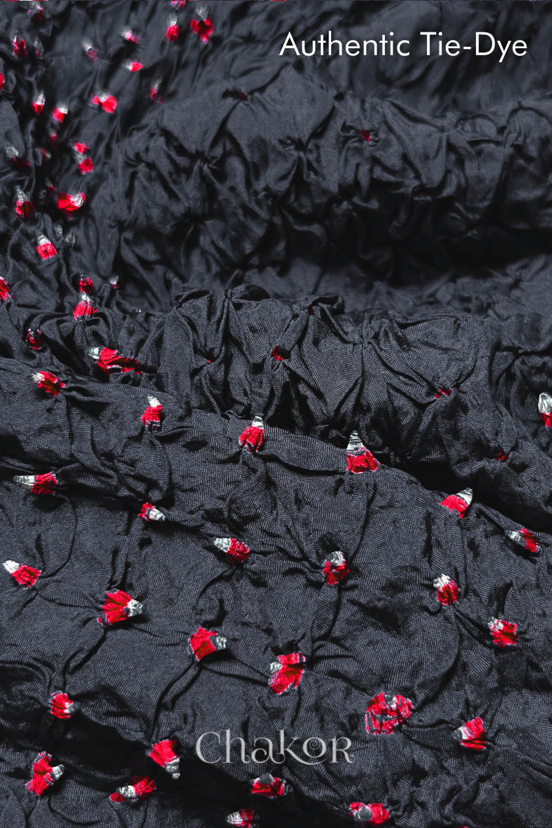 Close-up of Charcoal Grey mulberry silk fabric with Red and white patterns, featuring texture of authentic bandhani patterns.
