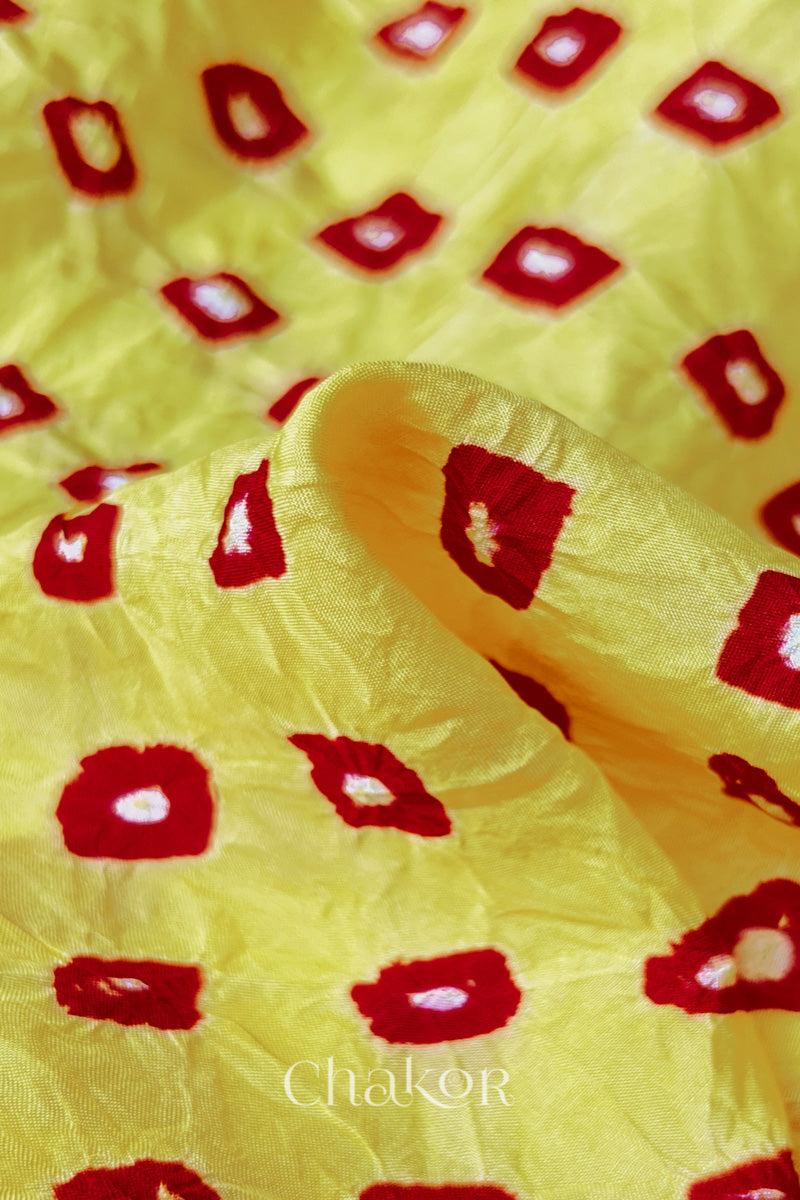 Close-up of yellow fabric with red and white bandhani patterns, featuring texture and sheen of soft mulberry silk fabric.