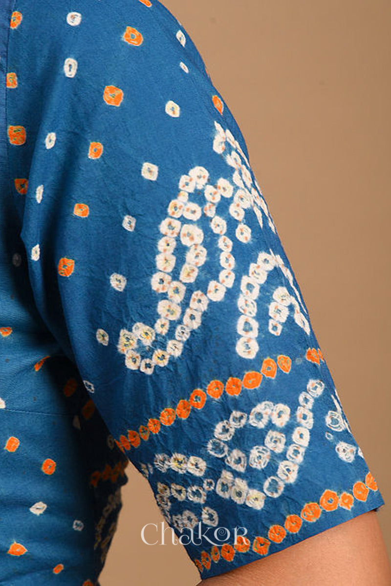 Woman wearing a handcrafted indigo blue bandhani cotton blouse with intricate parrot motifs and boria buttons on front.