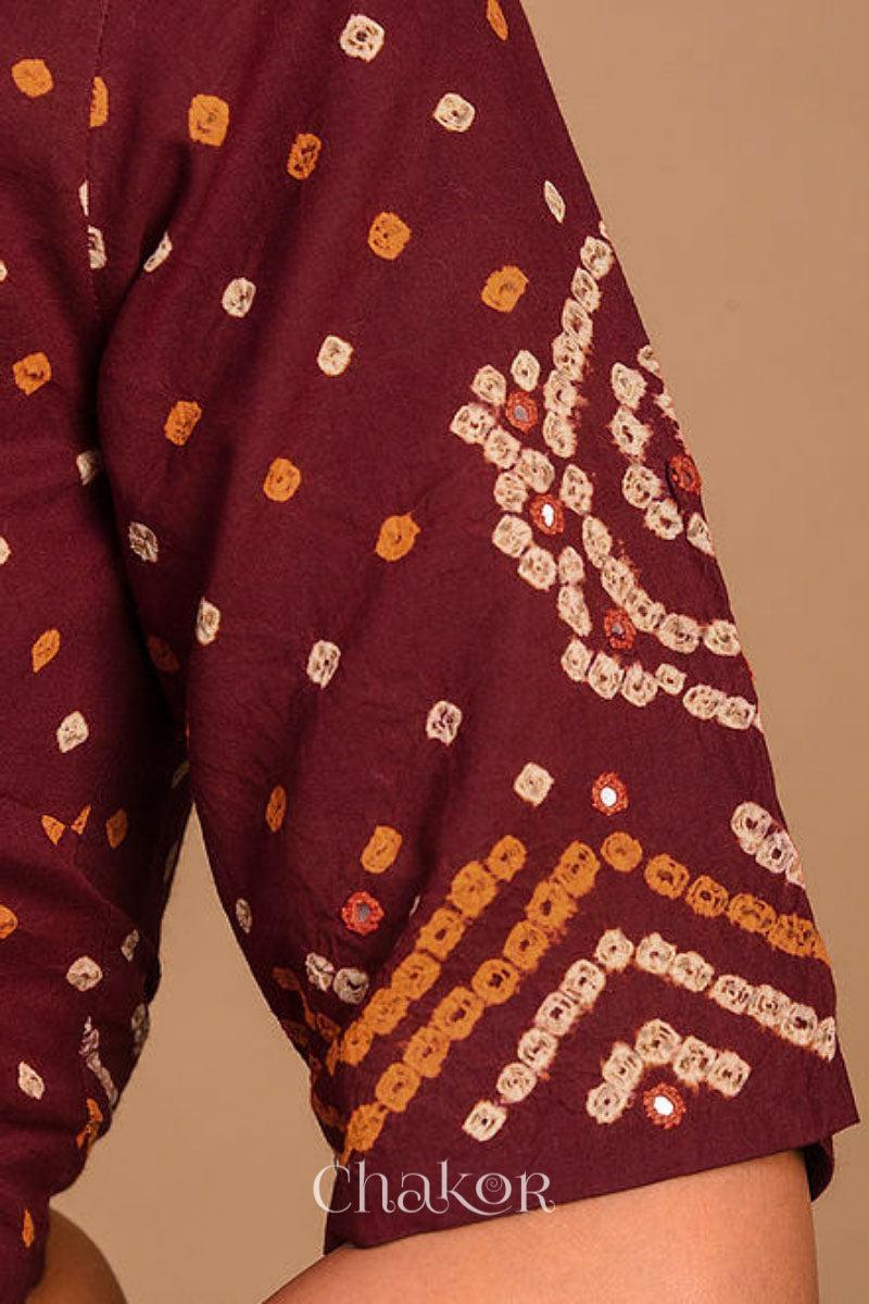 A woman wearing a traditional Maroon Bandhani Cotton Blouse with intricate mirror embroidered Keri - Paisley motifs and boria fabric buttons.