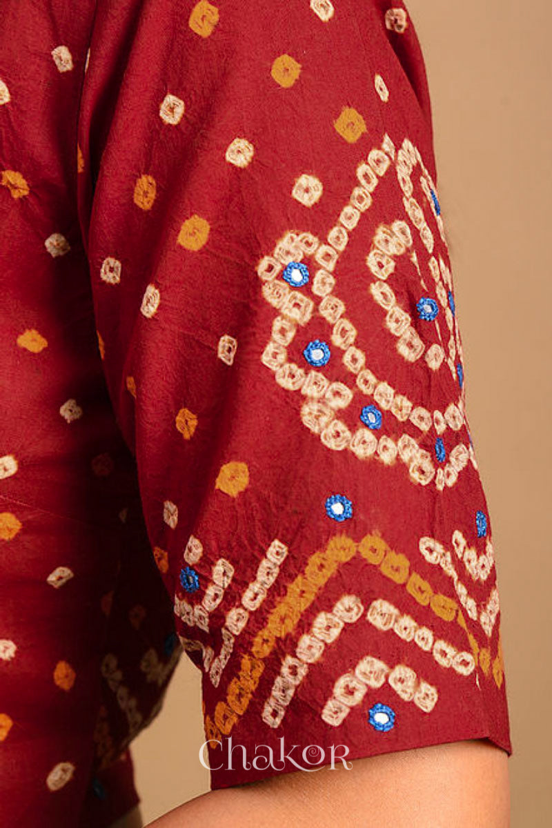 A woman wearing a traditional Red Bandhani Cotton Blouse with intricate mirror embroidered Keri - Paisley motifs and boria fabric buttons.